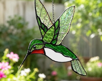 May include: A stained glass hummingbird suncatcher featuring vibrant green wings with textured glass, a bright red throat patch, and a white belly. The bird is outlined in black metal solder and hangs from a silver-toned metal chain.