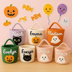 May include: A collection of Halloween-themed rope baskets in various colors, each with a name, a jack-o'-lantern or ghost design. Decorative stickers of pumpkins, candy, and balloons are arranged on a pink background.