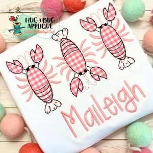 May include: White t-shirt with three pink and white gingham lobster appliques and the name "Maileigh" embroidered in pink.