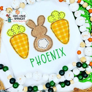 May include: A white onesie with a brown bunny, two orange carrots with green tops, and the name "PHOENIX" embroidered in green.