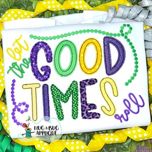 May include: A white t-shirt with a colorful embroidered design that says "Let the good times roll". The design features purple, green, and yellow colors and is surrounded by a beaded border.