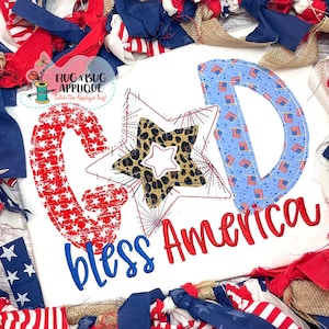 以下が含まれることがあります： 赤と青で「GOD bless America」と書かれた白いTシャツ。文字は星やストライプなど、愛国的な模様で装飾されています。真ん中にはヒョウ柄のデザインの星があります。Tシャツは赤、白、青の生地で囲まれています。