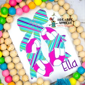 May include: Embroidered design of a pink and white bow with a pair of turquoise and white striped ballet shoes. The name "Ella" is embroidered below the shoes.