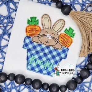 May include: Embroidered design of a brown bunny rabbit peeking out of a blue and white checkered pot with two orange carrots. The pot has the name "Brody" embroidered on it.