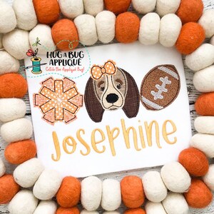 May include: Embroidered design featuring a brown and white dog with a pink bow, a football, and a orange and white starburst. The name Josephine is embroidered in yellow below the design.