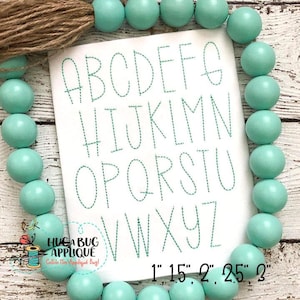 May include: A white card with a green stitched alphabet in various sizes from 1 inch to 2.5 inches. The card is surrounded by a turquoise beaded garland.
