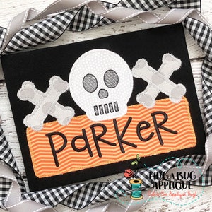 May include: A black and orange applique with a white skull and crossbones design. The name "Parker" is stitched in black on a banner below the skull and crossbones.