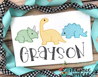 Könnte beinhalten: Ein weißer Strampler mit drei gestickten Dinosauriern in Grün, Gelb und Blau. Der Name Grayson ist unter den Dinosauriern gestickt.