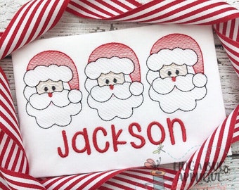 May include: White embroidered shirt with three red Santa faces and the name "Jackson" in red lettering.