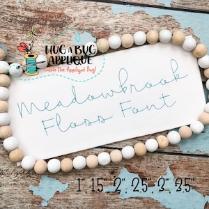 Puede incluir: Una tarjeta blanca con texto azul que dice "Meadowbrook Floss Font" con una cadena de cuentas de madera blancas y marrones alrededor de la tarjeta. La tarjeta también tiene el texto "Hug a Bug Applique" y "Catch the Applique Bug!" en texto más pequeño. La tarjeta tiene medidas indicadas en la parte inferior: 1", 1,5", 2", 2,5", 2", 3,5".