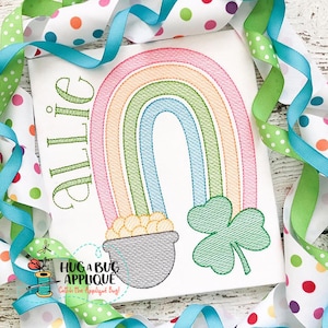 May include: A rainbow with a pot of gold and a shamrock at the bottom. The name "Allie" is stitched in green above the rainbow.