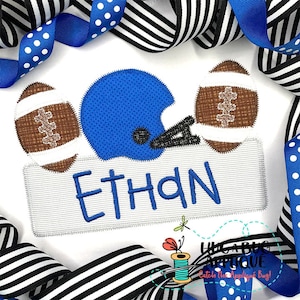 May include: A white t-shirt with a blue football helmet, two brown footballs, and a gray banner with the name "ETHAN" embroidered on it.