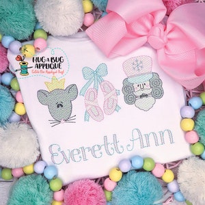May include: White onesie with embroidered images of a mouse, ballet shoes, and a nutcracker. The onesie has the name "Everett Ann" embroidered on the bottom.