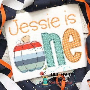 May include: A white onesie with the text "Jessie is one" in orange embroidery. The number one is made of teal fabric with a white star pattern and orange fabric with white polka dots. A striped pumpkin is embroidered in the bottom left corner.