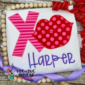 May include: A white t-shirt with a pink and white striped letter X and a red and pink polka dot lips applique. The name "Harper" is embroidered in purple below the applique.