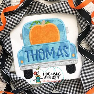 May include: A blue pickup truck with a pumpkin in the bed. The truck has the name "THOMAS" written on the back. The truck is on a white background.