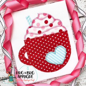 May include: Red and white applique design of a hot chocolate mug with whipped cream and a heart. The mug is decorated with small white hearts and the whipped cream is decorated with pink and red polka dots. The heart is blue with white stripes.