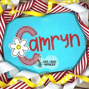 Könnte beinhalten: Hellblaues Applikationsdesign mit dem Namen "Camryn" in roter Schrift. Der Buchstabe "C" ist mit einem rot-weiß karierten Muster und einer weißen Gänseblümchen verziert. Das Bild ist mit roten, weißen und gelben Bändern umrahmt.