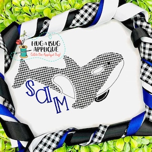 May include: A white t-shirt with a black and white gingham orca applique. The name "Sam" is embroidered in blue below the orca. The t-shirt is surrounded by black and white gingham ribbon.
