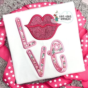 Puede incluir: Una camiseta blanca con una aplicación floral rosa y verde de la palabra "LOVE" con un diseño de labios de purpurina rosa sobre la palabra. El texto "HUG A BUG APPLIQUE" está en la esquina superior derecha de la camiseta.