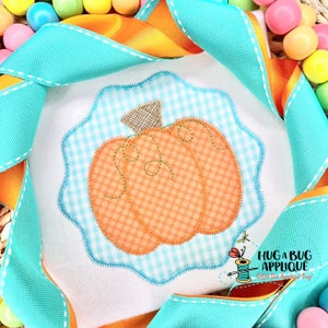 May include: A light blue and white gingham pumpkin applique with a brown stem. The applique is surrounded by a scalloped edge and is on a white background.