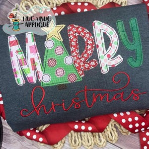 May include: Dark gray Christmas-themed shirt with the words "MERRY Christmas" in a festive design. The letters are decorated with gift boxes, floral patterns, and a Christmas tree. Red script lettering adds a decorative touch.