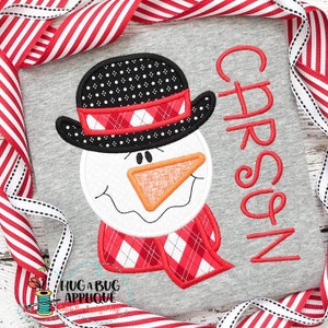 May include: A gray shirt with a red and white plaid scarf, a snowman face with a black hat, and the name "Carson" embroidered in red.
