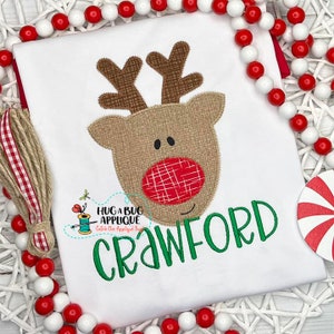 May include: A white t-shirt with a brown and red reindeer applique and the name "Crawford" embroidered in green.
