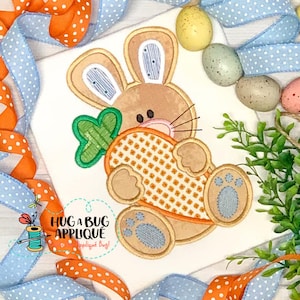 May include: Embroidered applique design of a brown bunny holding a carrot. The bunny has blue eyes and a green carrot top. The design is perfect for Easter crafts.