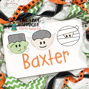 May include: A white t-shirt with three embroidered Halloween characters: a Frankenstein, a vampire, and a mummy. The name "Baxter" is embroidered below the characters in orange thread.