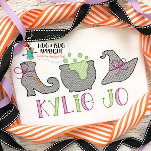 May include: Embroidered Halloween design featuring a witch's boot, cauldron, and hat with the name "Kylie Jo" stitched in purple and green thread.