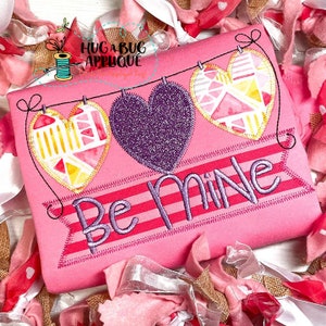 May include: Pink shirt with a purple, yellow, and pink heart banner that says "Be Mine".