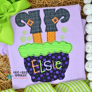 May include: Purple and black cauldron with green and white striped rim and a witch's legs sticking out of the top. The cauldron has the name "Elsie" embroidered on the front.