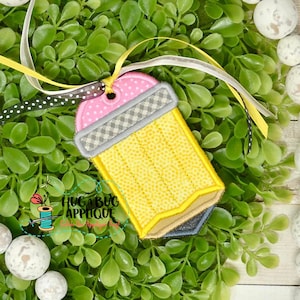 May include: A yellow pencil-shaped tag with a pink eraser and grey and white checkered pattern. The tag is attached to a white ribbon with black polka dots.