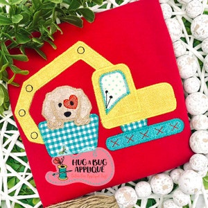 Könnte beinhalten: Eine gestickte Applikation eines Hundes, der in einem gelben Bagger fährt, mit einem roten Herzen auf der Brust des Hundes. Die Applikation befindet sich auf einem roten Stoffhintergrund. Der Text "HUG A BUG APPLIQUE" ist in der unteren rechten Ecke des Bildes sichtbar.