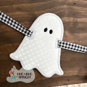 May include: White ghost-shaped applique with black eyes and a gingham ribbon. The ghost has a polka dot pattern and a white stitched outline. The applique is part of a Halloween-themed craft project. The text "HUG A BUG APPLIQUE" is visible.