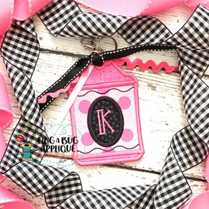 May include: Pink and black fabric crayon keyring with a white letter K in the centre. The keyring is decorated with white polka dots and a scalloped edge.