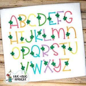Peut inclure: Alphabet brodé aux couleurs vives, orné de trèfles verts. Les lettres sont cousues sur un tissu blanc. L'image comprend le texte "HUG A BUG APPLIQUE" et un dessin d'une bobine de fil.