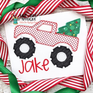 Puede incluir: Camión monstruo rojo con neumáticos negros transportando un árbol de Navidad verde con luces amarillas. El camión tiene un patrón de cuadros rojos y blancos. El nombre Jake está bordado debajo del camión.