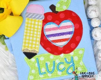 May include: A blue shirt with an applique design of a red apple with a heart inside, a yellow pencil, and a green banner with the name "Lucy" on it.