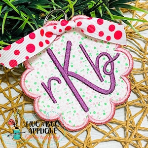 May include: A pink and white scalloped fabric keychain with a purple embroidered monogram "rk" and a pink and white polka dot ribbon bow.