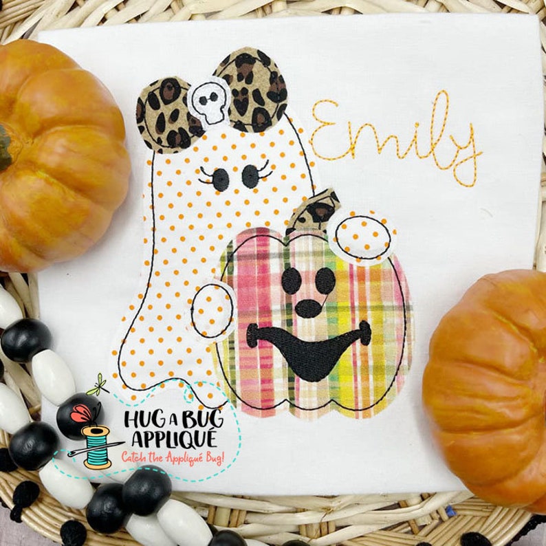 May include: A white ghost with orange polka dots and a leopard print bow holding a plaid pumpkin with a jack-o-lantern face. The name "Emily" is embroidered in orange thread on a white background.