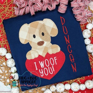 May include: A blue t-shirt with a red heart and a brown and white dog applique. The heart has the text "I woof you!" on it. The name "Duncan" is embroidered on the side of the shirt.