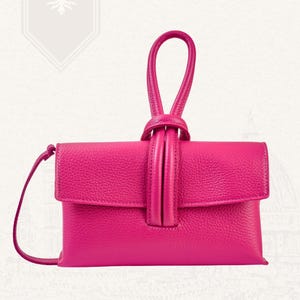 May include: A vibrant fuchsia leather clutch with a top handle and a detachable shoulder strap. The bag features a flap closure and a textured surface. The words "VITA DI LUSSO" are printed at the top right.