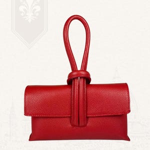 May include: A red leather clutch bag with a looped handle. The bag has a flap closure and a textured surface. The handle is knotted at the top. The brand name "VITA DI LUSSO" is visible in the top right corner.