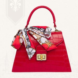 Peut inclure: Un sac à main rouge avec une finition texturée, doté d'une poignée supérieure et d'un fermoir doré. Un foulard à motifs rouge, blanc et noir est noué à la poignée. Le sac a une forme trapézoïdale structurée.