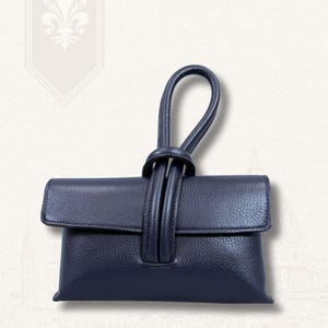 May include: A navy blue leather clutch with a knotted handle. The clutch has a flap closure and a textured surface. The words "VITA DI LUSSO" are printed in gold at the top right.