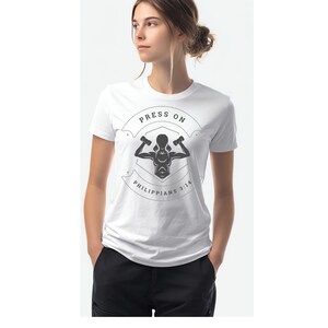 May include: White t-shirt with a graphic design featuring a weightlifter and the words "PRESS ON" above and "PHILIPPIANS 3:14" below. The shirt is short-sleeved and has a crew neck.