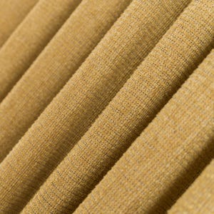 Peut inclure: Gros plan sur un tissu texturé de couleur jaune doré chaud. Le matériau est plié en diagonale, créant un effet côtelé. Le tissu a un aspect tissé, avec une texture visible et de subtiles variations de couleur.