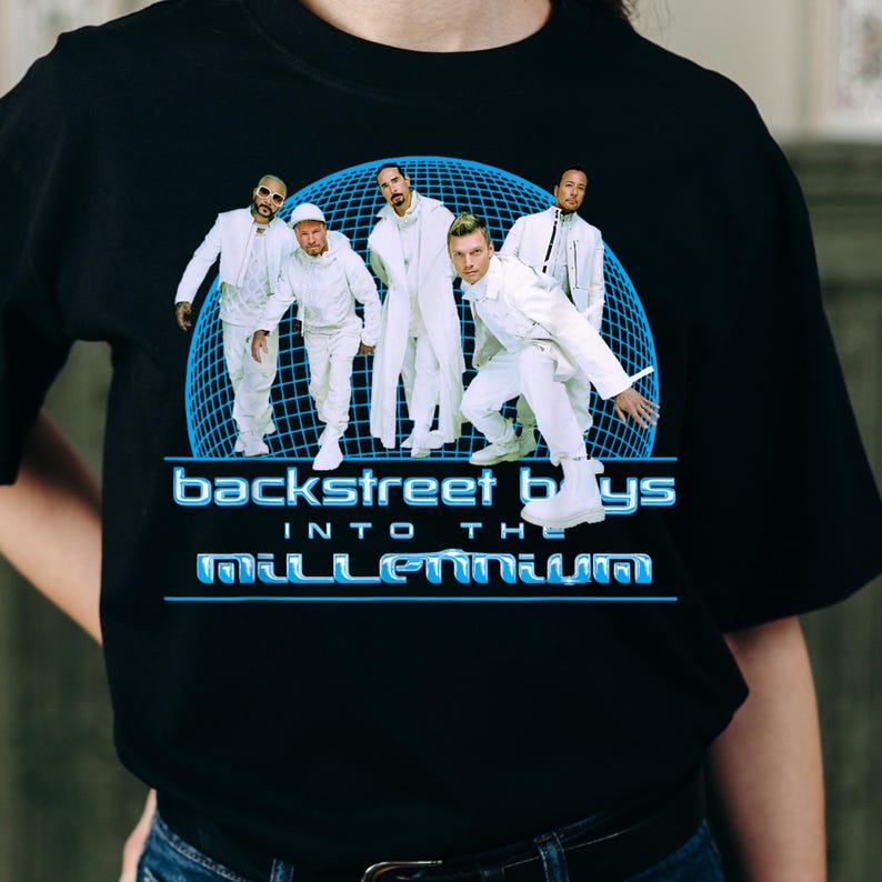 May include: A black t-shirt featuring a graphic of the Backstreet Boys in white outfits against a blue grid sphere. The text reads Backstreet Boys Into The Millennium in a blue font. The design is centered on the front of the garment.